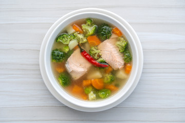Fresh salmon fish soup with carrots, potatoes, red peppers, green broccoli and onions in a white plate, close up. Tasty dinner consists of a fish soup with salmon