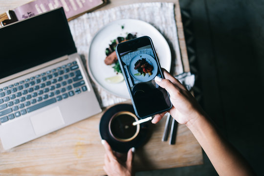 Faceless woman taking picture of food in restaurant