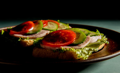 delicious sandwiches with ham, tomato, cucumber and lettuce on a green background