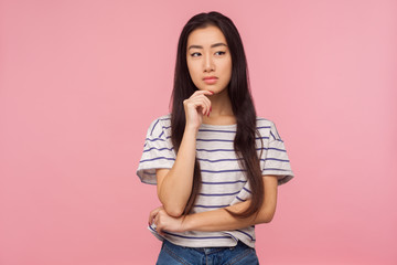 Portrait of cute pensive girl with long hair in striped t-shirt pondering decision, looking confused uncertain, having doubts while thinking over solution. studio shot isolated on pink background