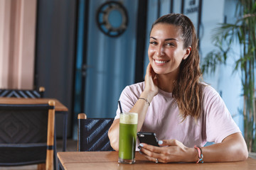 Attractive smiling woman on vacation, enjoying paradise resort, sit in cafe using mobile phone and drinking healthy smoothie, look camera, self-care time alone, travel blogger write post internet