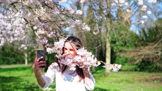 Beautiful young woman takes phone selfie with cherry tree. Close up parallax shot