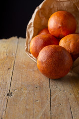 Close-up of blood oranges in paper bag, with selective focus, on rustic wooden board and black background, vertical, with copy space