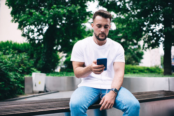 Man using smartphone and listening to music while sitting on bench