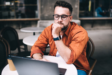 Pensive freelancer working on laptop while sitting in cafe