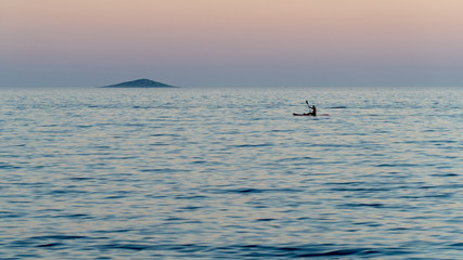 Canoeist sailing alone on the calm sea at dusk.