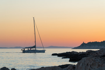 Yacht at sea floating on the rocky coast at dusk.