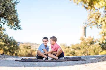 Fototapeta premium Two boys sitting on the floor in nature playing, hugging, and laughing. Siblings connection.