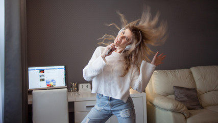 cheerful girl with a phone and big headphones is dancing and singing. Holds the phone as a...