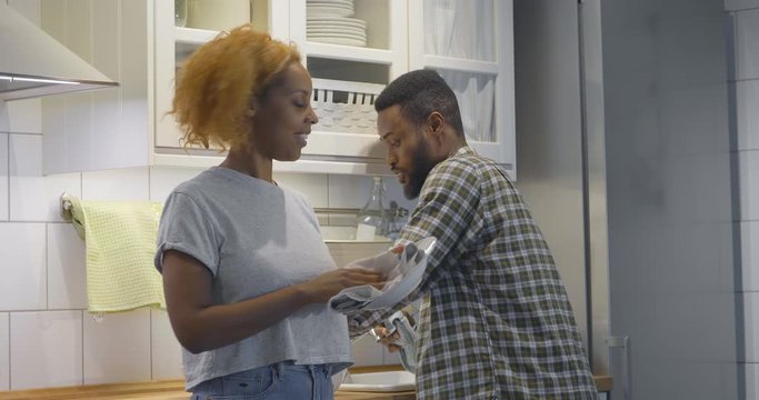 African couple wiping dishes with towels and chatting in kitchen