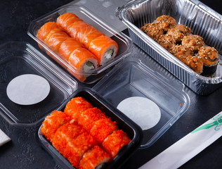 set of  rolls with delivery in containers, Philadelphia rolls with salmon, California with caviar, baked with eel, Japanese food on a black background, sticks, top view,