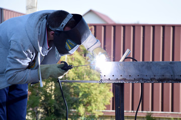 Man in protecting welding helmet mask grey sweater with zipper dark blue pants and gauntlet work...