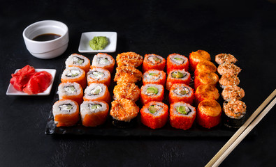 set of Japanese rolls  California with caviar,   Philadelphia with salmon,baked with cheese and eel, wasabi, pickled ginger, soy sauce on a black ,  lots of sushi