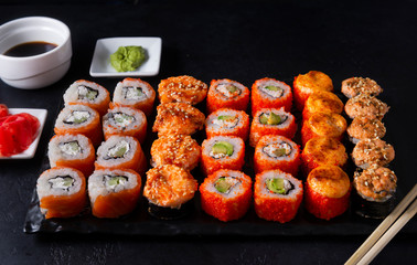 lots of sushi , set of Japanese rolls  California with caviar,   Philadelphia with salmon,baked with cheese and eel, wasabi, pickled ginger, soy sauce on a black , sticks,