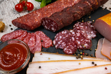 abstract background with smoked sausage with sauce, cherry tomatoes and basil on a black graphite board. top view