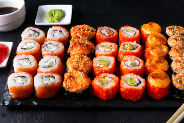 many sushi , set of Japanese rolls  California with caviar,   Philadelphia with salmon,baked with cheese and eel, wasabi, pickled ginger, soy sauce on a black , sticks,