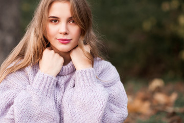 Beautiful teen girl 17-18 year old wearing cozy sweater posing outdoors over nature background. Looking at camera. Childhood.
