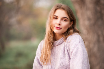 Beautiful blonde teen girl 16-18 year old wearing knitted sweater posing outdoors over nature background. Looking at camera. Spring season.