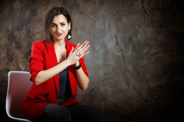 Attractive woman in a red jacket sitting against a dark wall. Young mysterious girl. Dark tones. Copy space