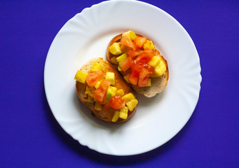 White bread bruschetta sandwiches with tomato and zucchini on a white plate on a purple background, top view