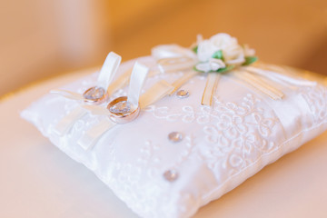 Obraz na płótnie Canvas golden wedding rings on small white leather cushion
