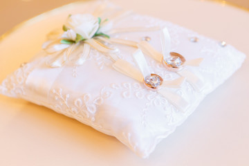 golden wedding rings on small white leather cushion