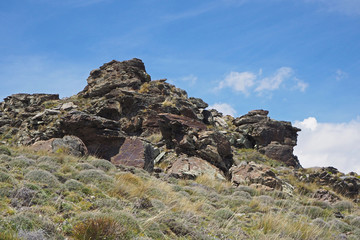The mountain landscape with the slope covered by green grass, the big dark rocks, blue sky with white clouds on the sunny spring day.