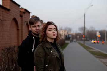Young beautiful girl standing with his back to the guy. Young loving couple on background of brick wall.