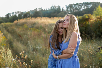 horizontal closeup portrait of two cute adult sisters on a background of grassy slope in the countryside