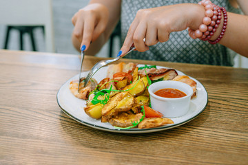 Female hands with knife and fork cut chicken in bacon. Chicken, potatoes and sauce. Female hands with manicure and bracelet
