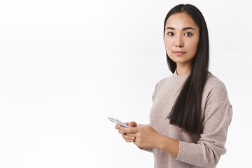 Good-looking elegant young modern asian woman coworker in beige sweater, holding smartphone turn...
