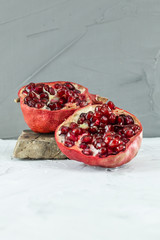 Halved red ripe pomegranate on the little grey stone isolated on light textured background, natural...