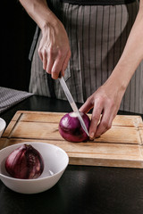Female graceful hands cut red onion on a cutting board. Chef at work in the kitchen. Vertical shot