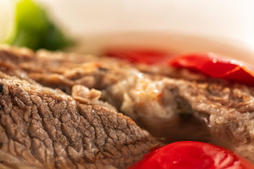 Shorpo in a white plate with a piece of beef meat in a broth with vegetables close up