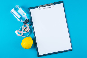 The diet plan. White sheet on the tablet among the bottles with water and apples with measuring...