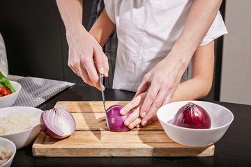 Women's and children's hands cut red onions together. Cooking with kids is tasty in the restaurant