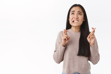 Troubled, worried cute asian girl in beige blouse, have concernes, cross fingers good luck, biting...