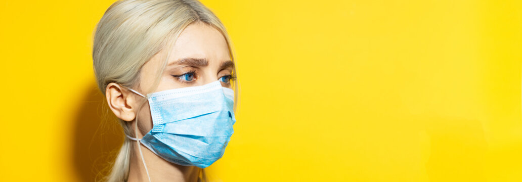 Panoramic portrait of young blonde girl with blue eyes, wearing medical face mask against coronavirus on yellow background with copy space. - Powered by Adobe
