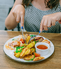 Woman in cafe tastes chicken in bacon and sauce. Meat, potatoes and sauce on a white plate. The knife and fork cut the dish
