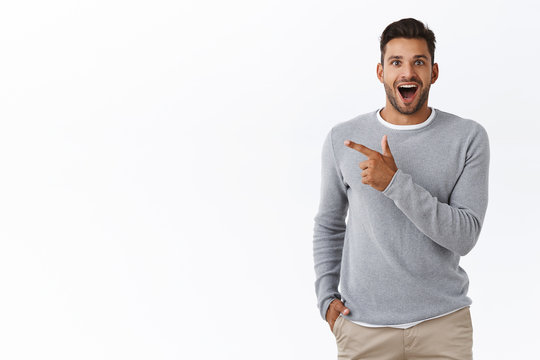 Fascinated happy and excited handsome young male coworker discuss boss new car, smiling impressed and amused, pointing left, standing surprised with astonished expression, white background