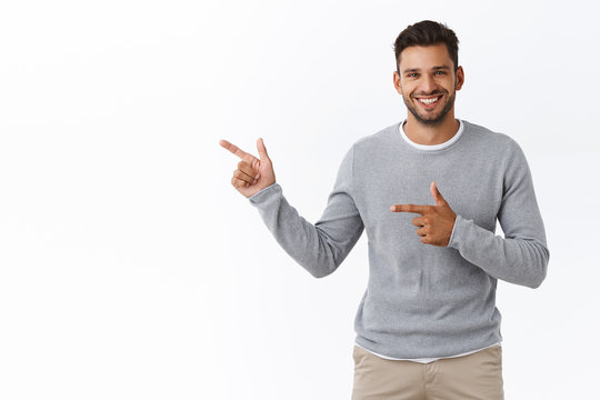 Good-looking charming bearded caucasian guy with short stylish hairstyle, wear grey sweater, pointing left, advertise product, corporate promotion, give advice or recommendation, smiling pleased