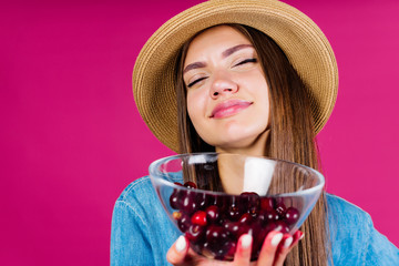 happy girl in a hat holds a plate with cherries on a pink background in the studio