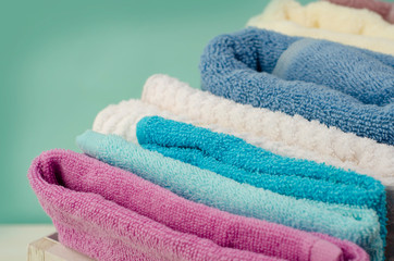 Bath towels of different colors in wicker basket on light background