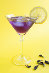 Iced blue flower tea with lemon in a martini  glass on the yellow background. Location vertical. Closeup.