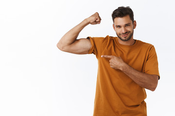 Sassy confident smiling macho man with big muscles, proudly pointing his hand as showing biceps on...