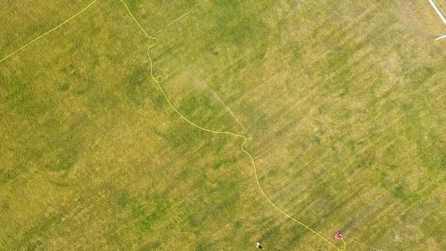 Top down aerial view of football field surface covered with green grass and sprinklers spraying water.