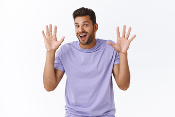 Fototapeta premium Cheerful enthusiastic modern guy in purple t-shirt have nothing hide, raising hands in surrender or retreatment, smiling joyfully, waving hands in hi, friendly greeting gesture, white background