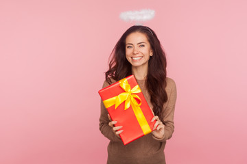 Portrait of happy beautiful angelic young woman with halo holding big present and smiling to...