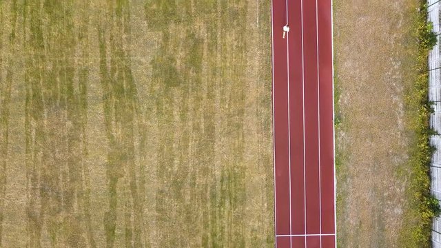 Top down aerial view of a jogger running on red football field tracks.
