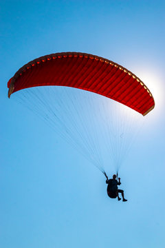The sun is shining through the red paraglide of an unrecognizable paraglider (silhouette).